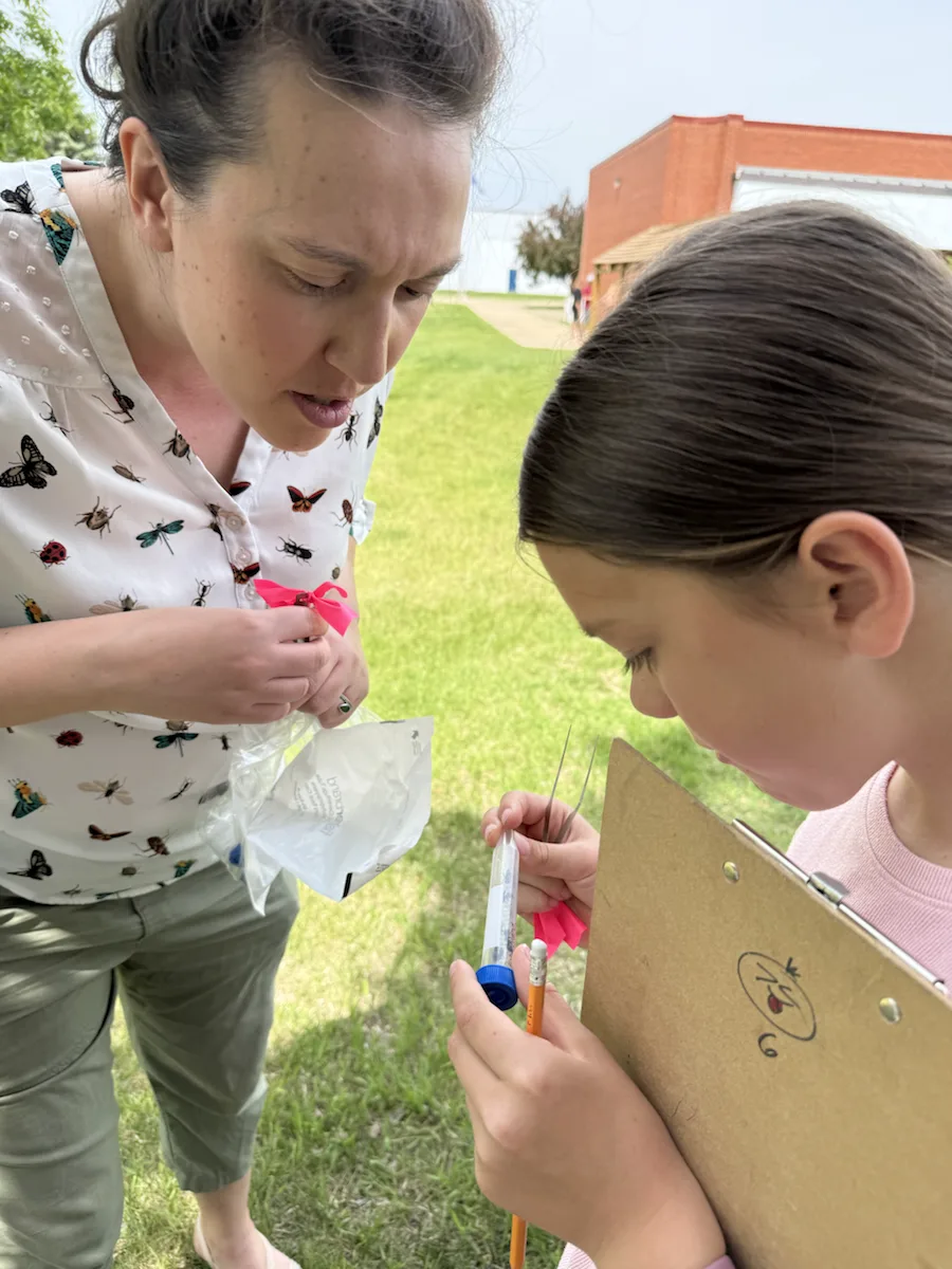 A student records observations on a clipboard alongside a researcher.