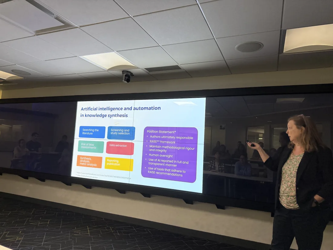 A speaker presenting a slide titled 'Artificial intelligence and automation in knowledge synthesis'.