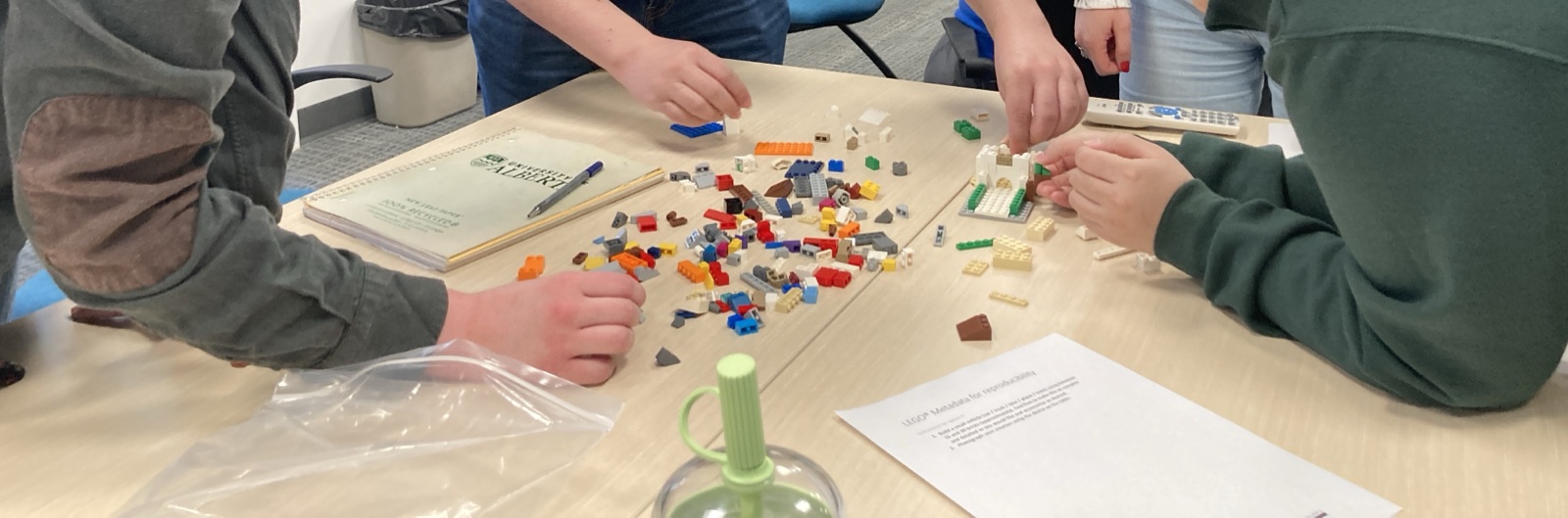 Canada-Wide Science Fair finalists collaborating around a table covered with LEGO bricks and worksheets.