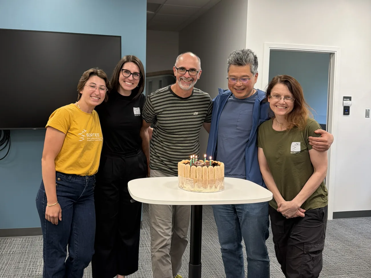 COSSEE members posed together behind the SORTEE birthday cake with lit candles.